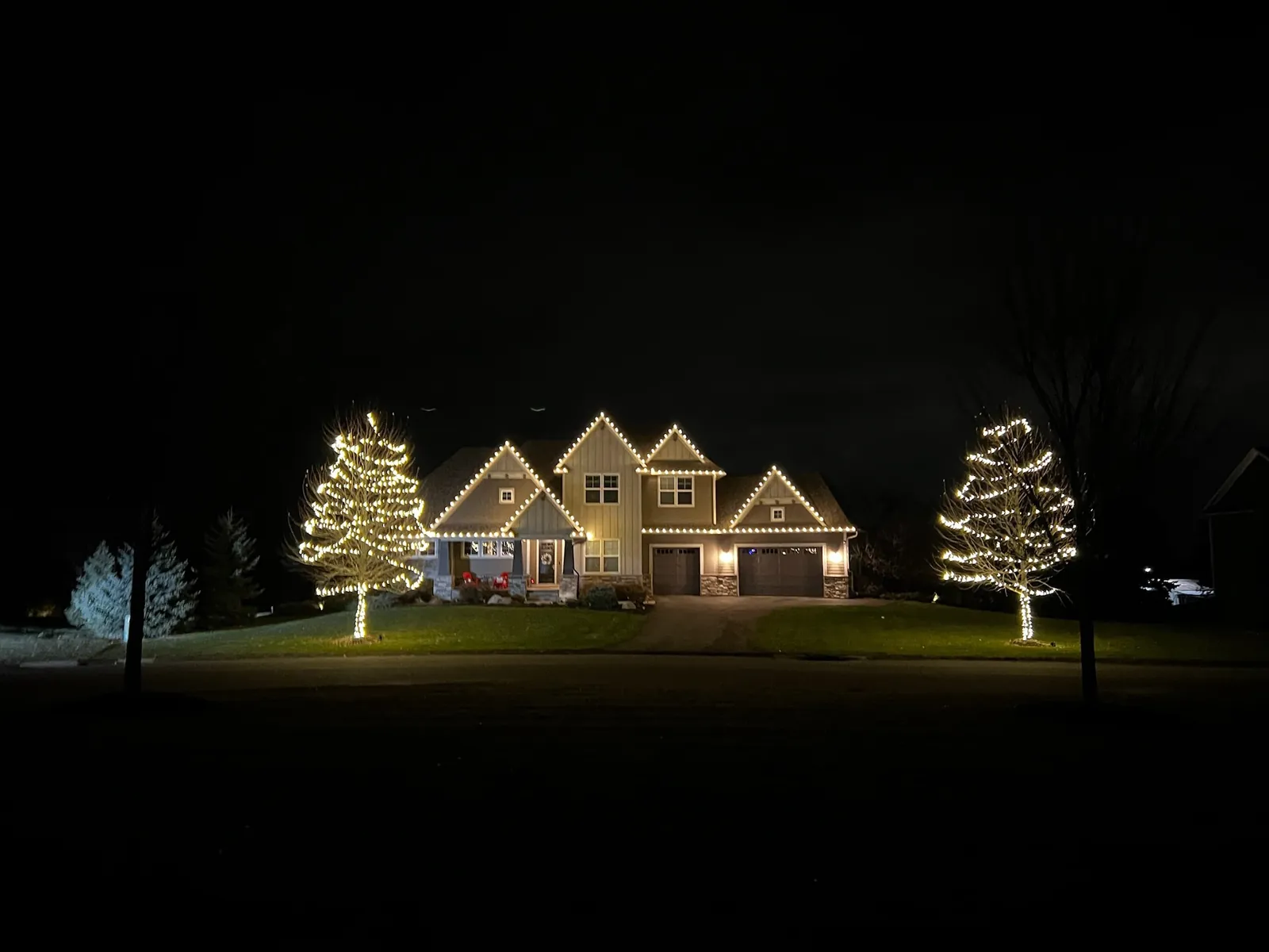 Two-storey home with lit rooflines and two wrapped trees on the lawn